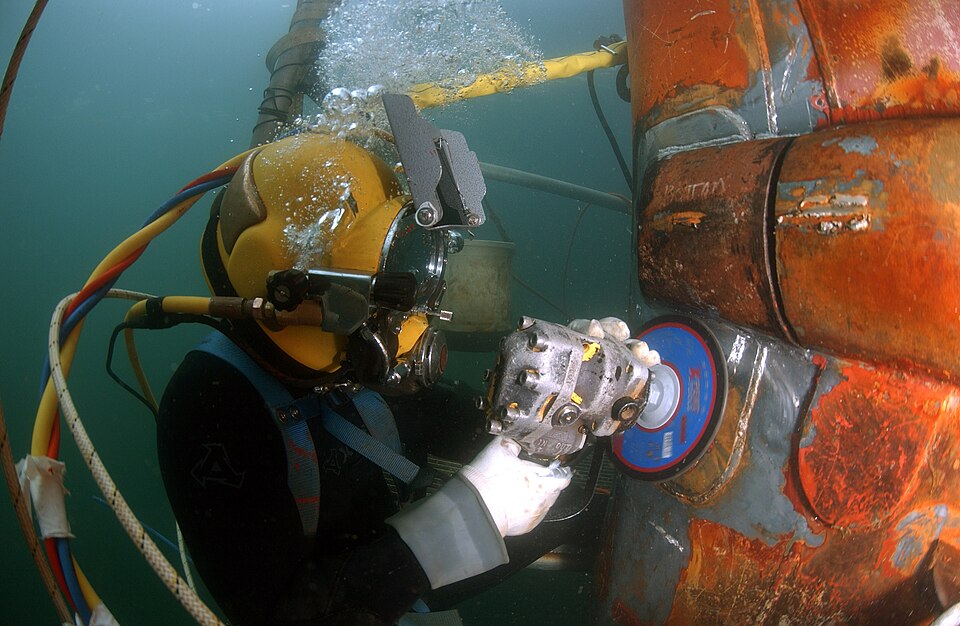 Historical photograph of a helmeted surface-supplied diver using a grinder on a ship hull in San Diego in January 2007.