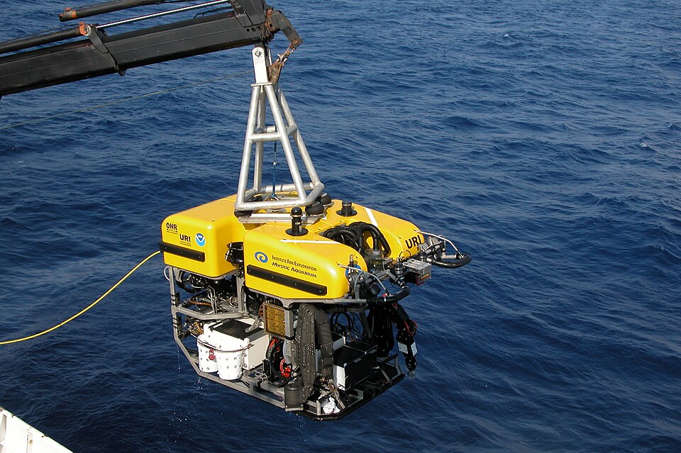 Archival photograph of the yellow Hercules research ROV suspended from a ship crane above the sea, identified by the creator as a 2005 launch.