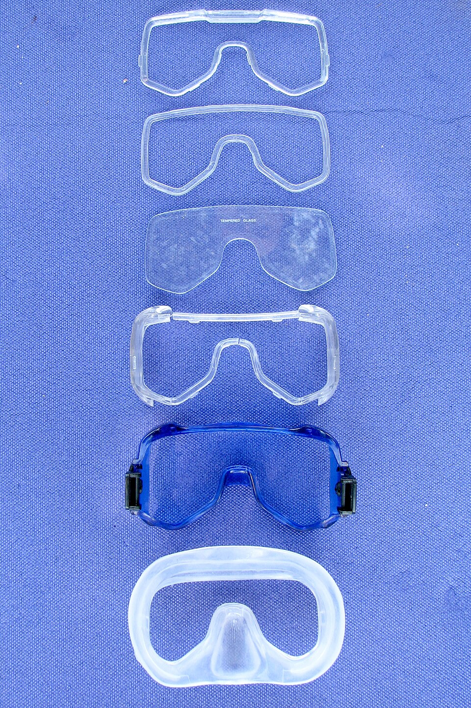 Disassembled conventional diving mask and its separate glass lens on blue cloth