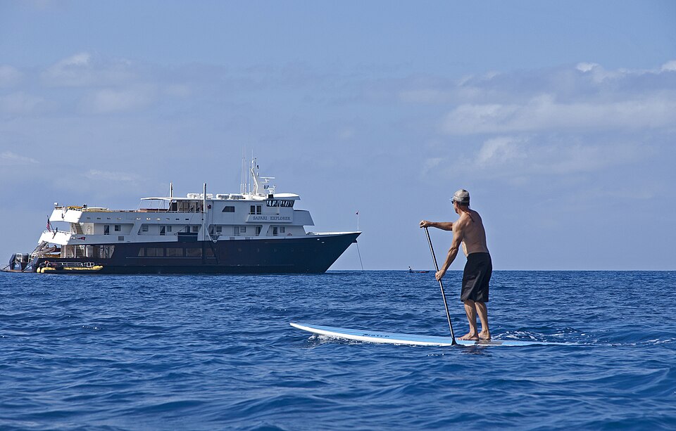 Paddleboarder on blue water near Safari Explorer