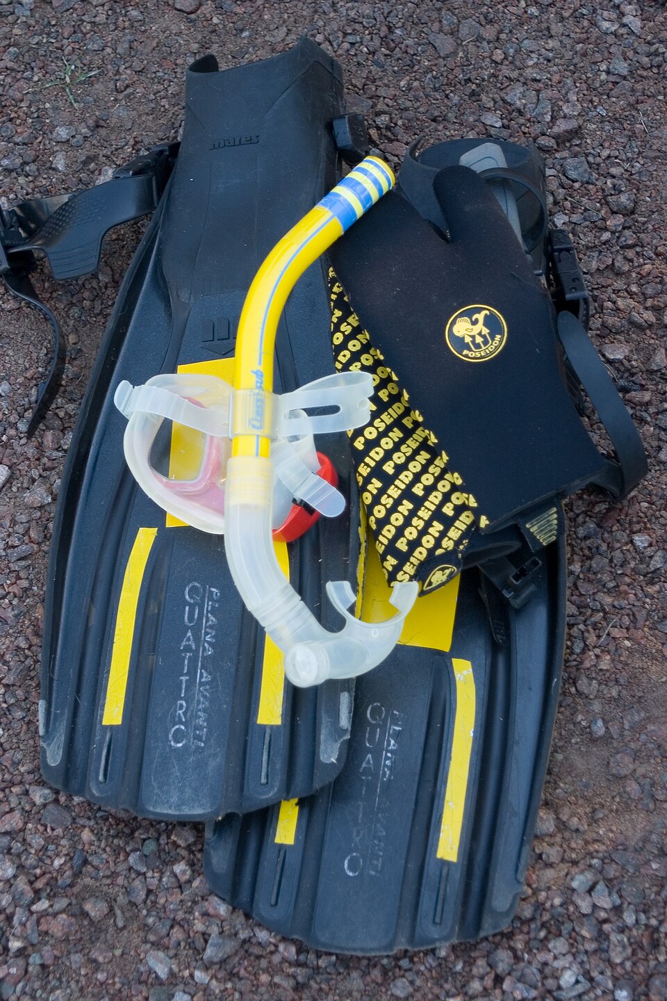 Fins, mask, snorkel and gloves arranged on a gravel surface