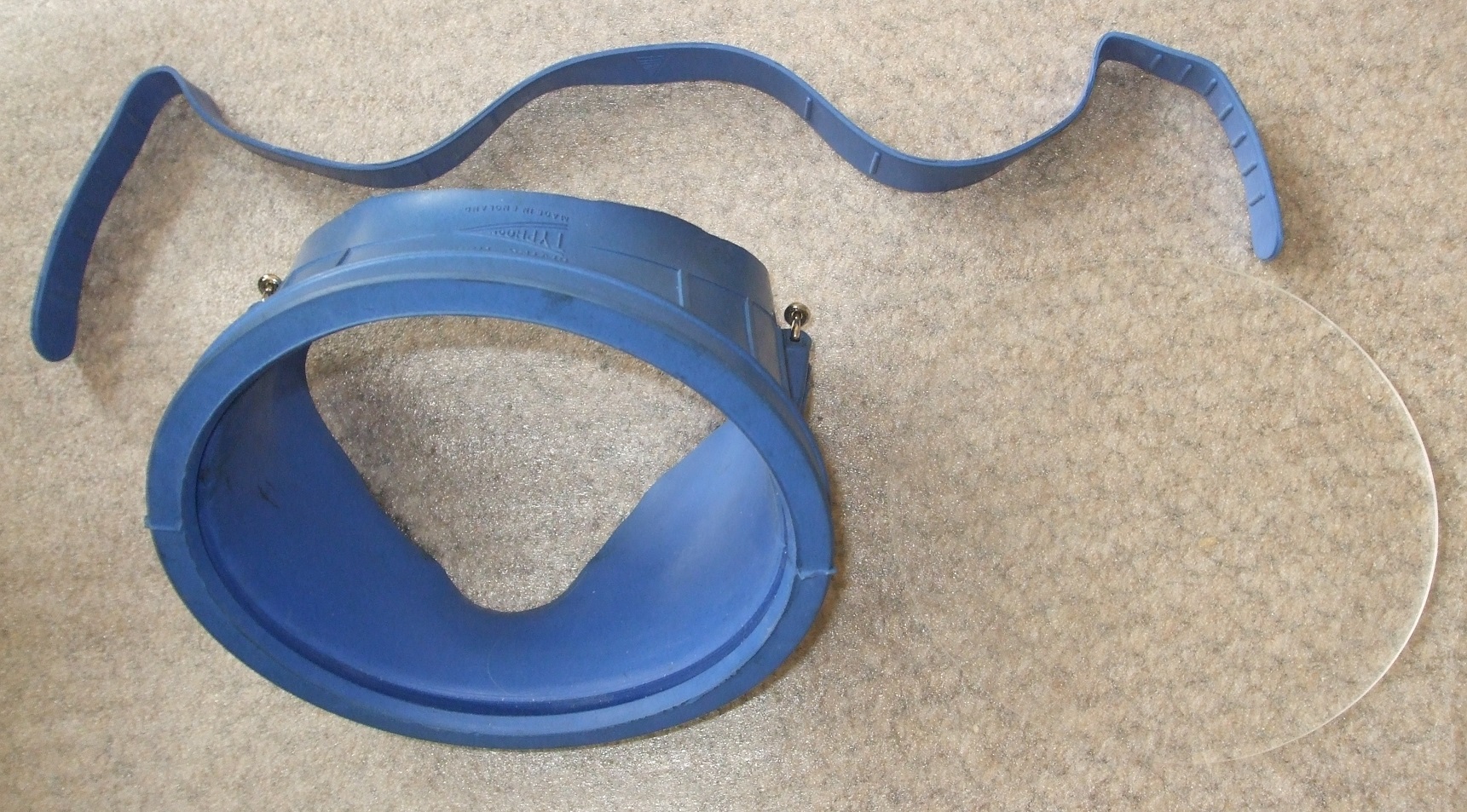 An older blue mask body, strap and separate single lens on a neutral surface