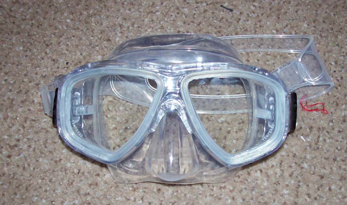 A diving mask with a clear skirt and strap on a textured surface