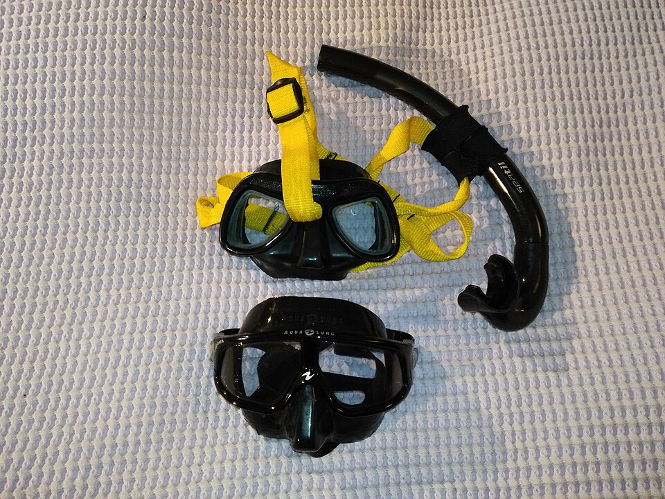 Two masks with different bands beside a snorkel on light fabric