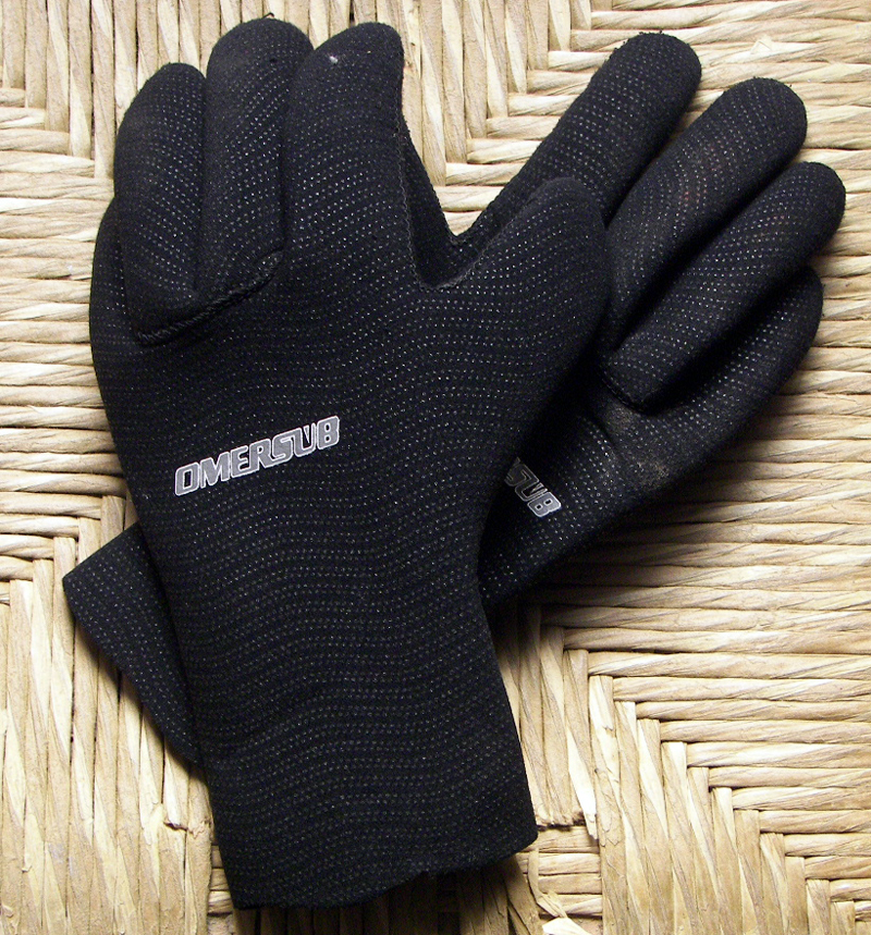 A pair of black neoprene diving gloves on a woven surface