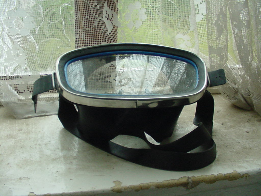 A single-window diving mask with a dark skirt and strap on a windowsill