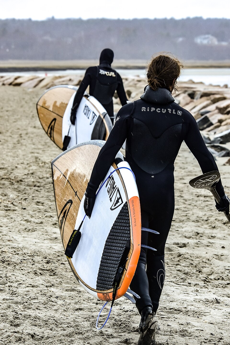 Surfers carrying boards along a beach in Wells