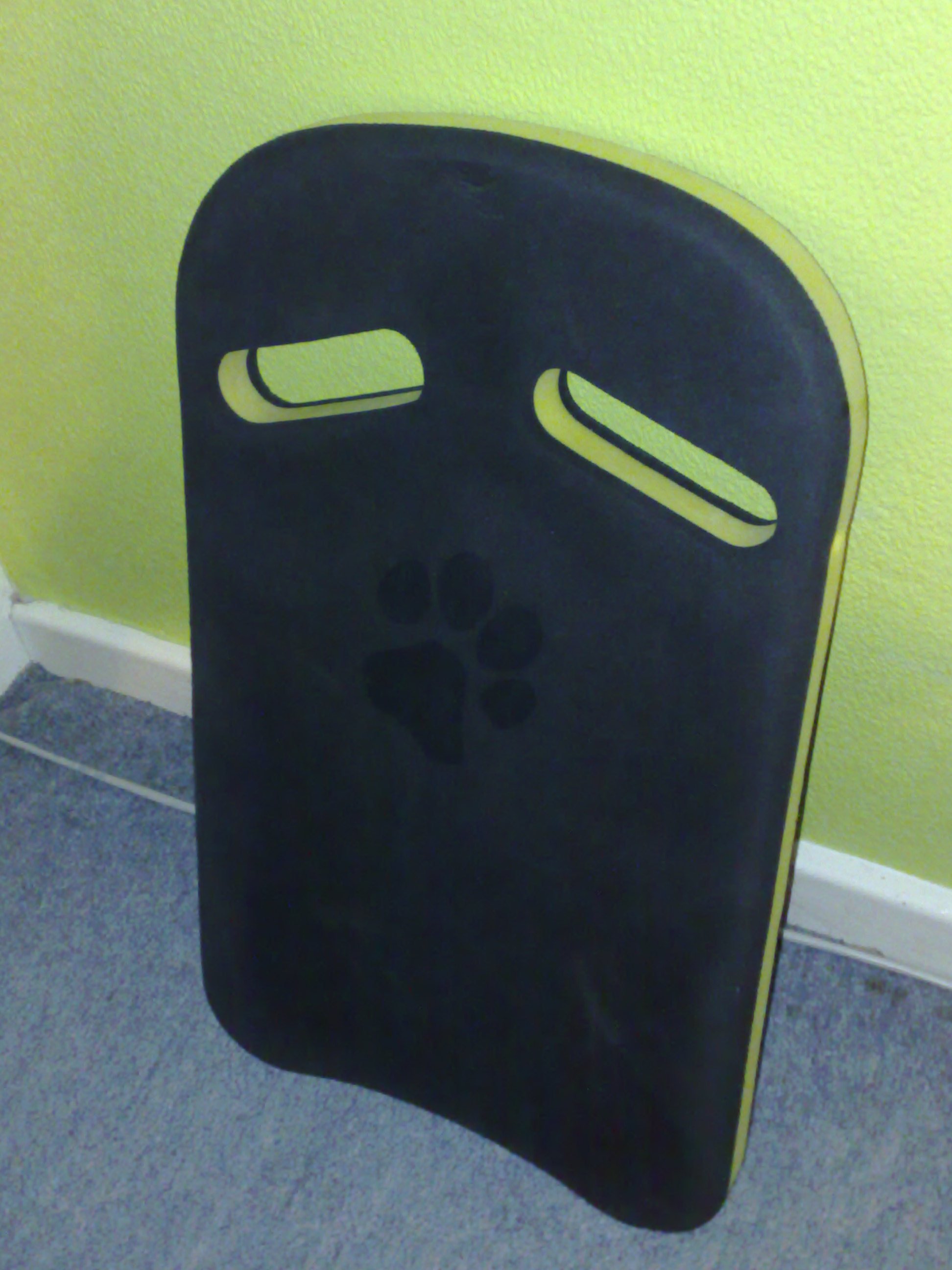 Archive black foam swimming kickboard with two hand openings leaning against a wall.
