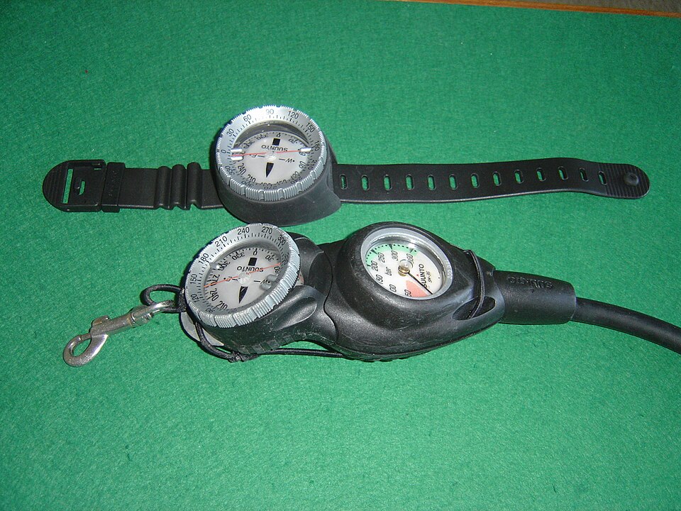 Archive photograph of a wrist-mounted dive compass above a console containing a compass and gauge.