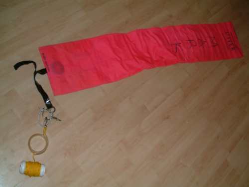 Archived photograph of an unfurled red marker buoy with attached line equipment on a floor.