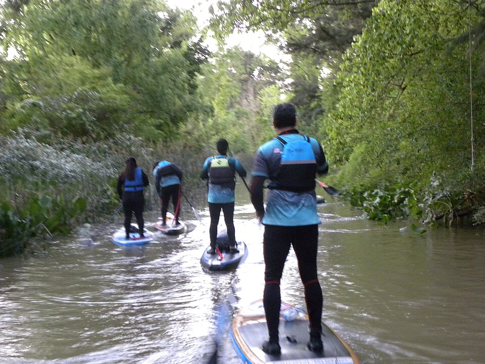 Back-view paddleboarders on a tree-lined waterway at Villa La Ñata