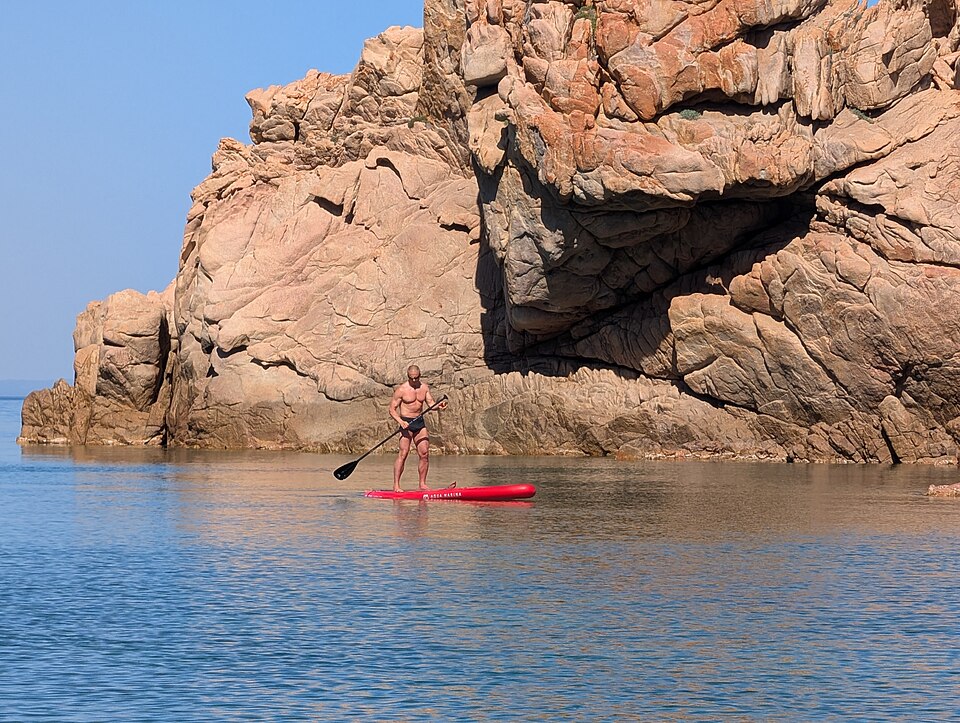 Paddleboarder on the water beside the rocks near Li Cossi beach