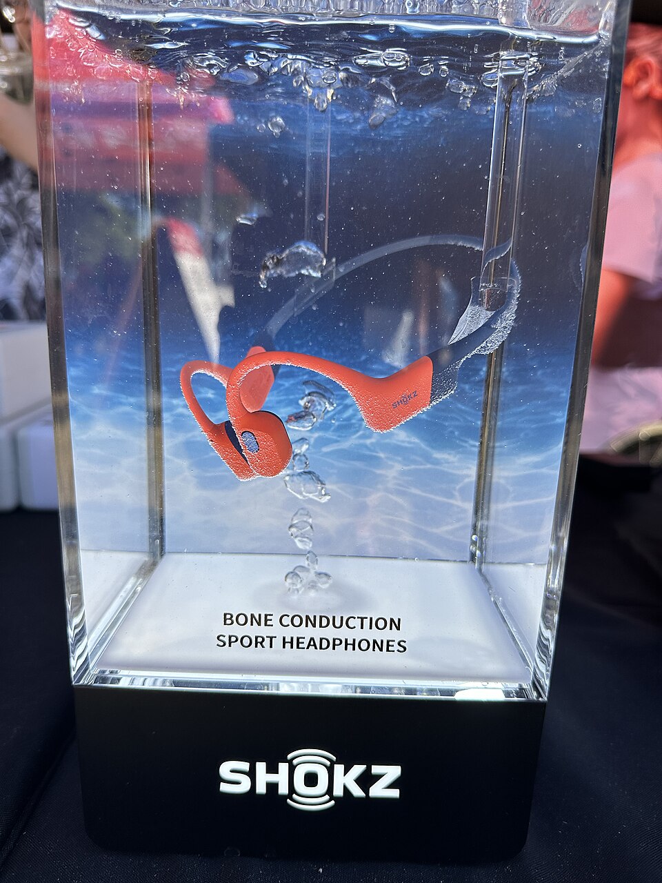 Archived photograph of an orange OpenSwim Pro headset inside a water-filled product-display container.